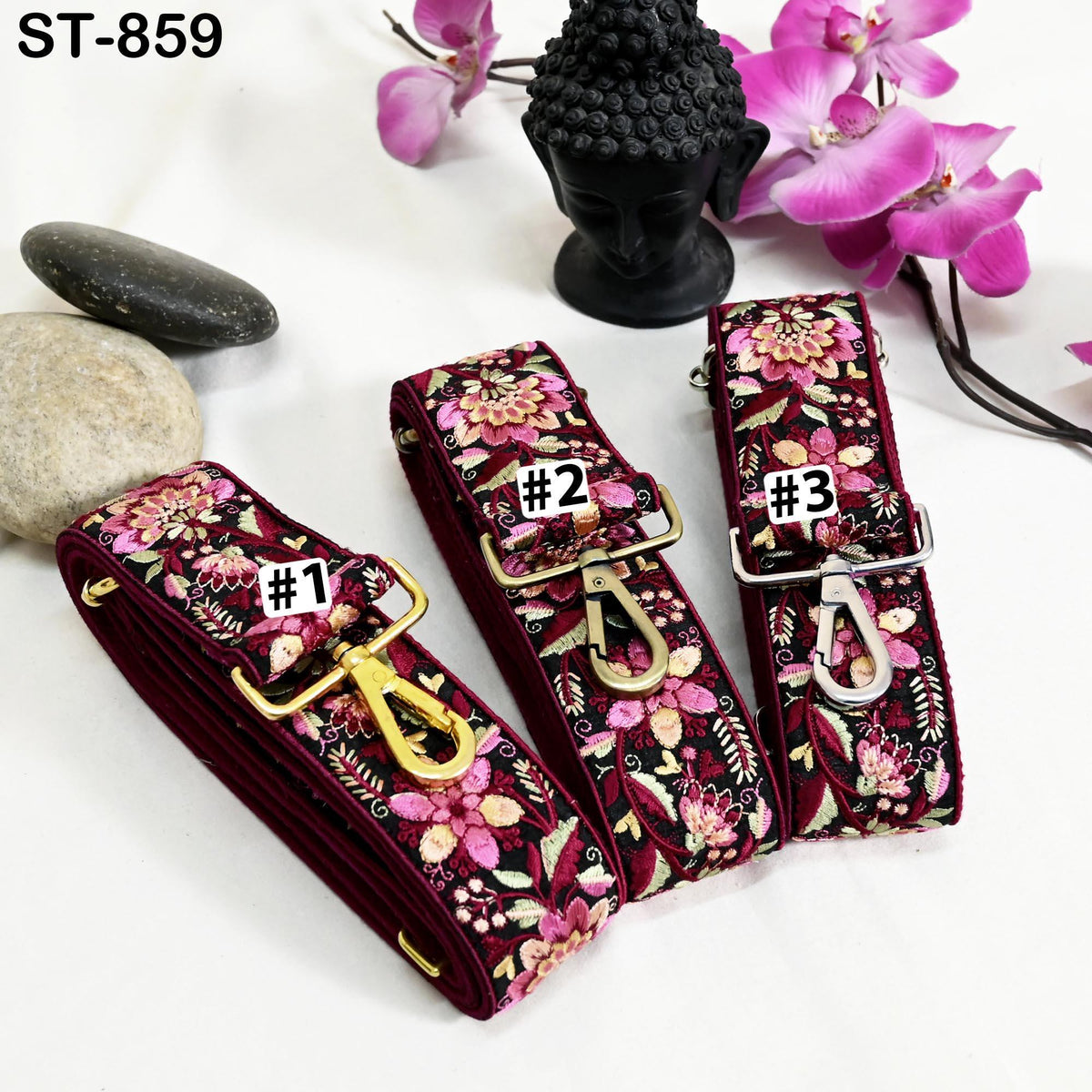 three colorful straps with floral patterns, each with a different number printed on it. The straps are placed on a white surface, with a black Buddha statue and pink orchids in the background.