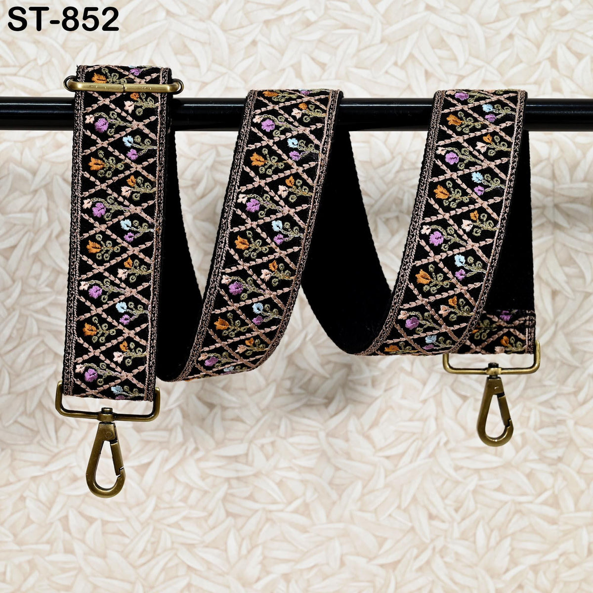 A decorative black strap with a floral pattern, featuring a gold-colored metal clasp and hook at the end.