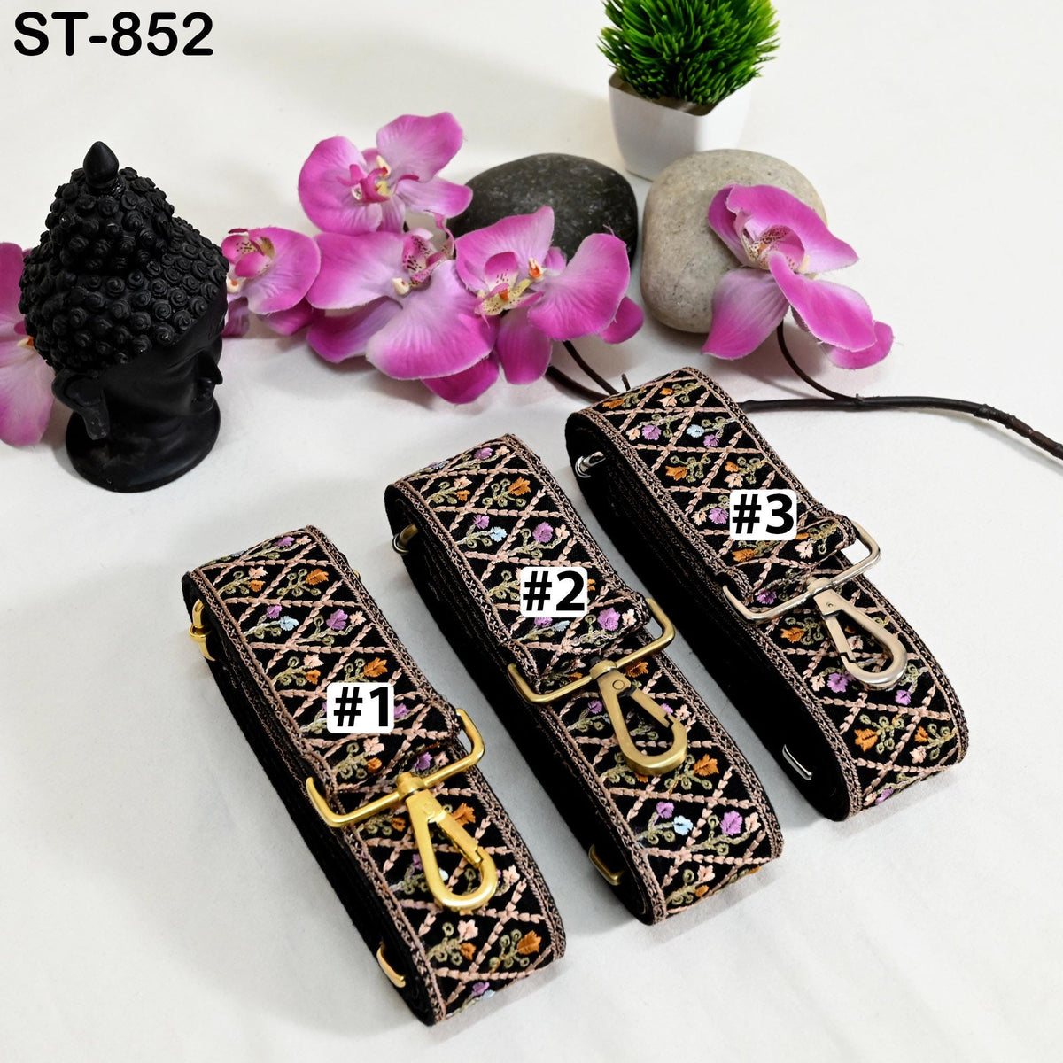 three colorful straps with numbers on them, placed on a white surface alongside a black Buddha statue, pink orchids, and a small potted plant.