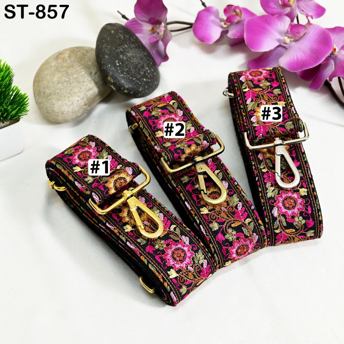 three colorful straps with floral patterns, each with a different number printed on it. The straps are placed on a white surface, with a few rocks and purple flowers in the background.