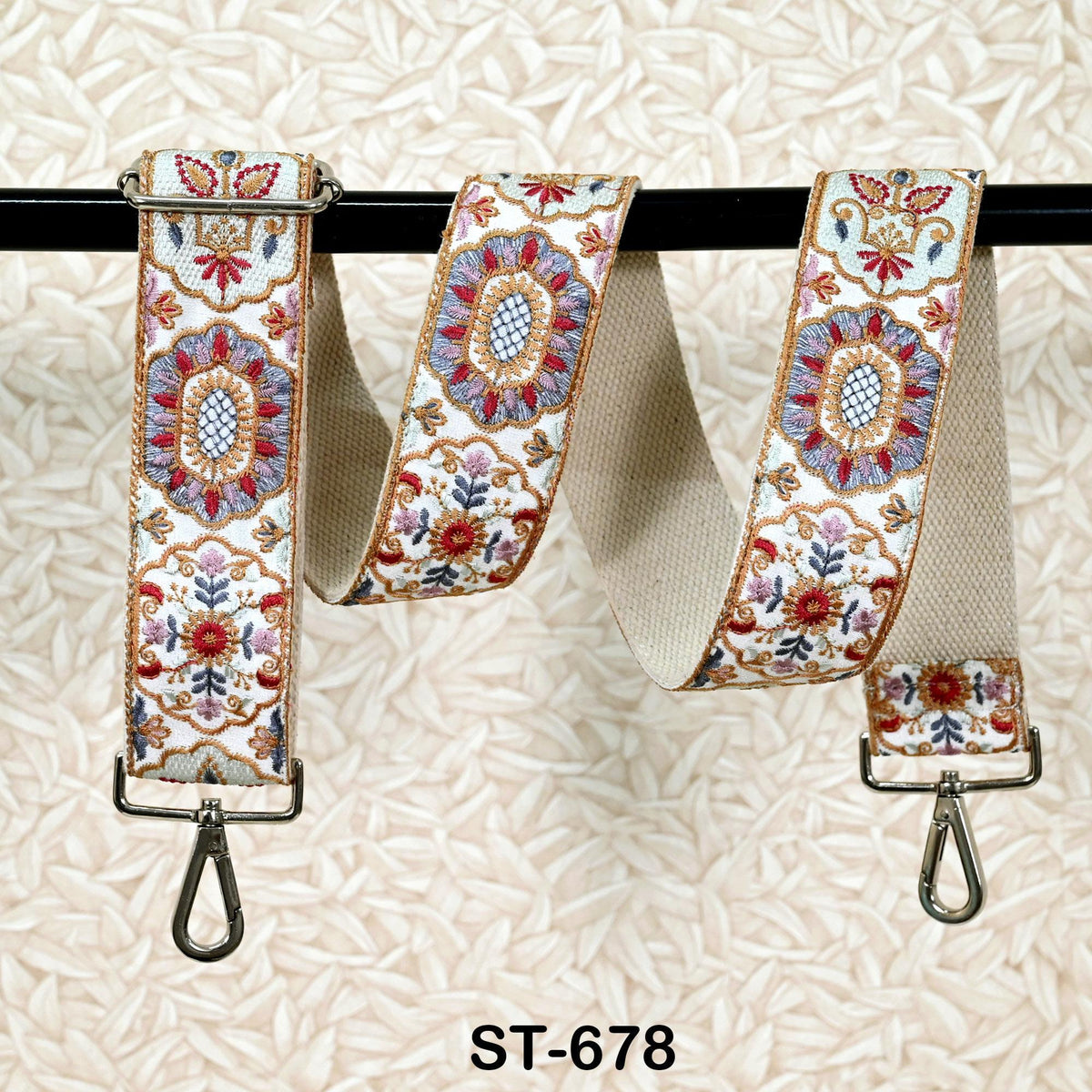 A decorative fabric strap with floral patterns, hanging from a black metal hook against a beige background.