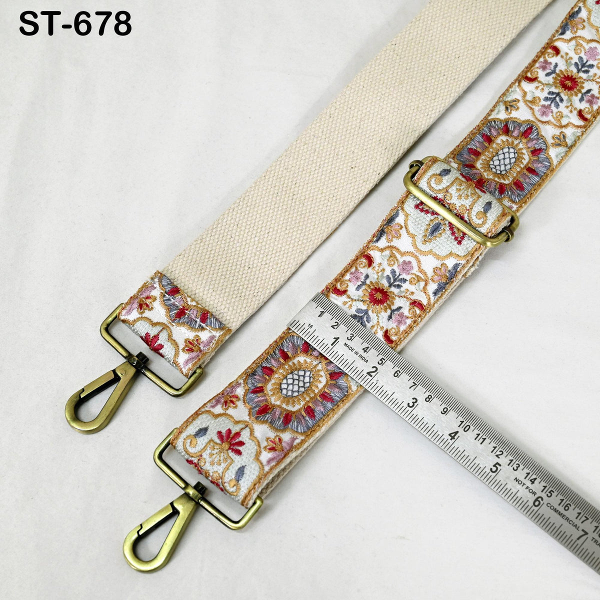 a beige strap with a floral pattern and two metal buckles, one on each end. A ruler is placed next to the strap, indicating the strap's length.
