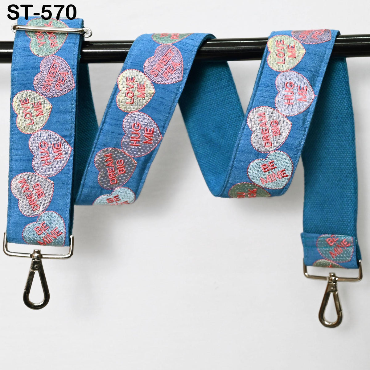A blue strap with heart-shaped embroidered designs and the words "Be Mine" printed on it.
