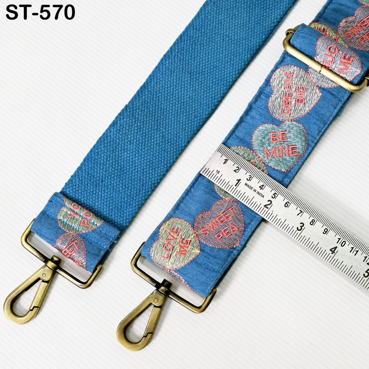 A blue strap with heart-shaped embroidered designs and a ruler for size comparison.