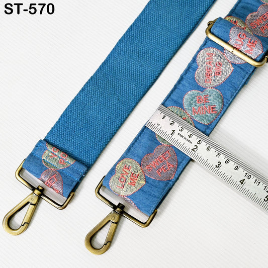 A blue strap with heart-shaped embroidered designs and a ruler for size comparison.