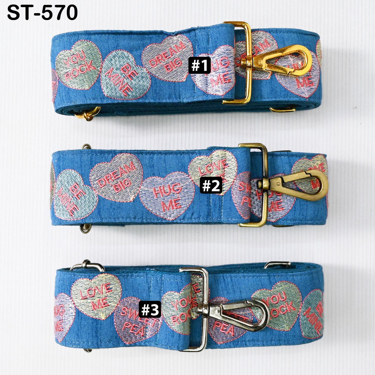 three blue straps with heart-shaped embroidered phrases on them. The straps have gold buckles and metal clips.