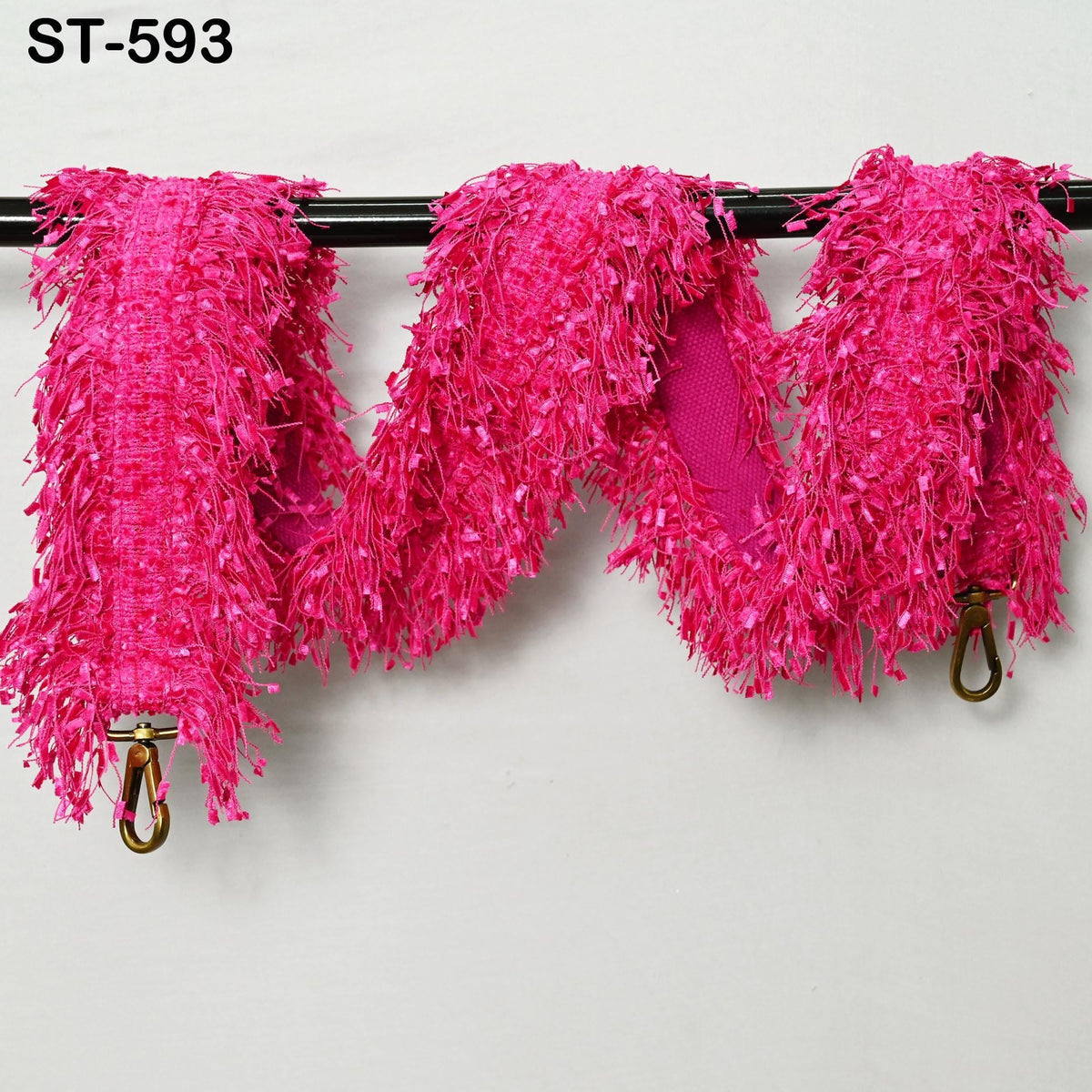 a pink, fluffy, and textured fabric item hanging on a black rod.