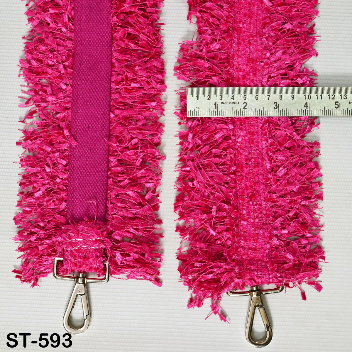 two pink straps with fringed edges, each attached to a metal hook. A ruler is placed between the straps, indicating the size or length of the straps.