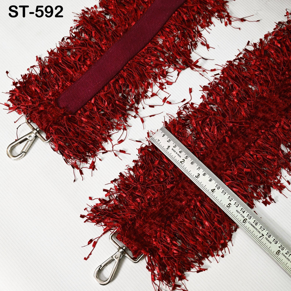 a red, fuzzy fabric with a metallic strap attached to it, and a ruler placed next to it, indicating the size or dimensions of the fabric.