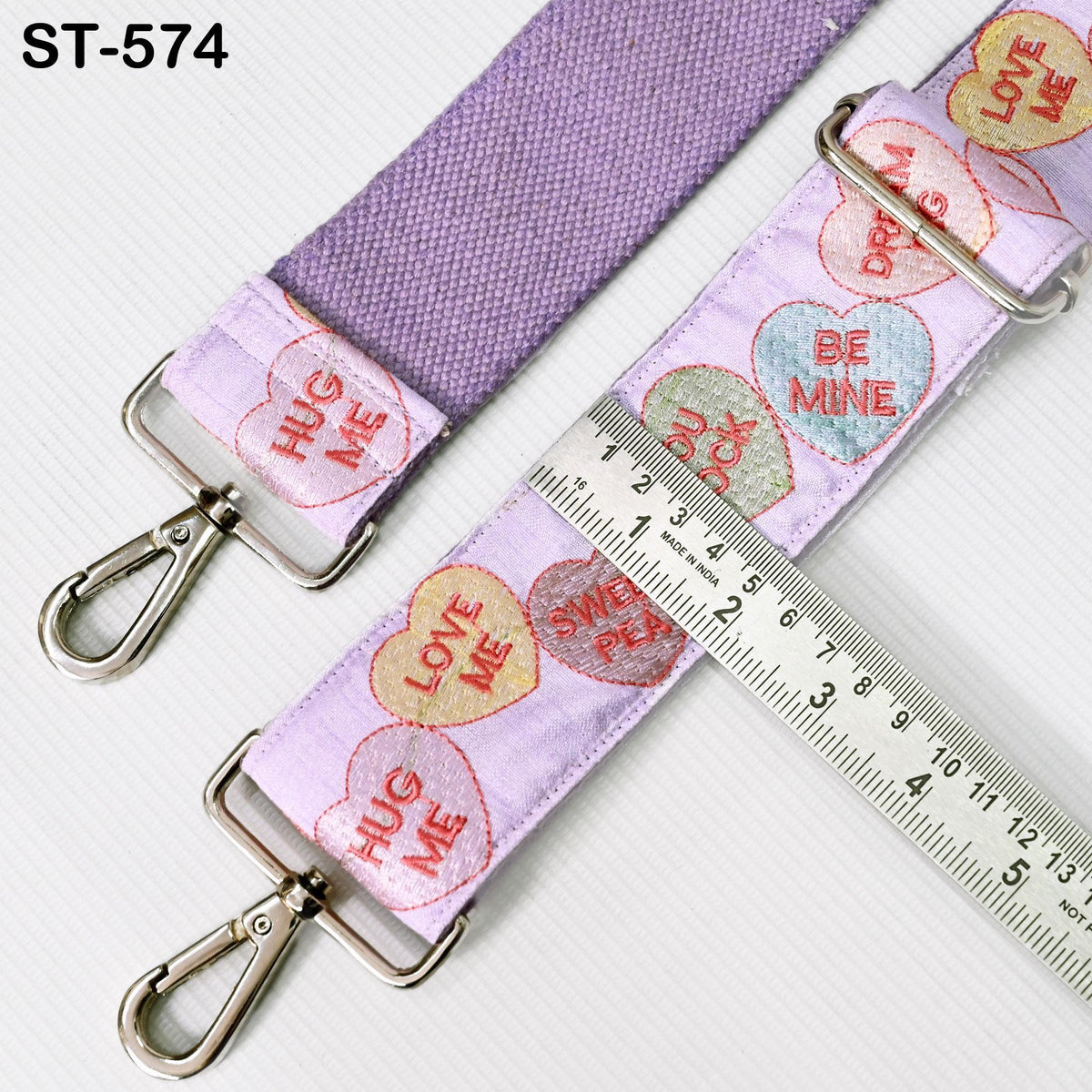 a purple strap with a heart-shaped embroidered pattern, and a ruler is placed next to it, indicating the strap's length.