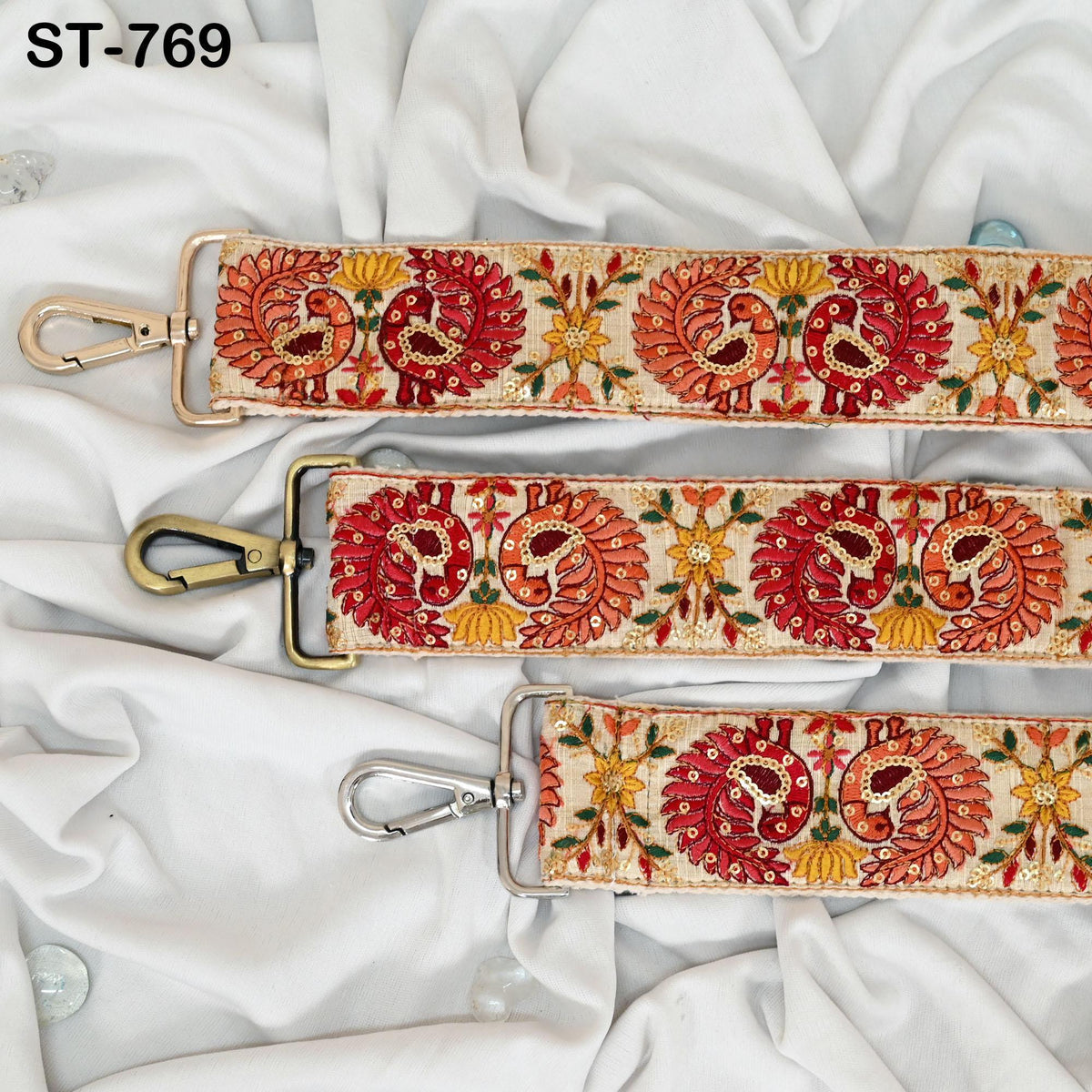 three decorative straps with intricate patterns in red, orange, and yellow colors. The straps appear to be made of fabric and are arranged on a white cloth background.