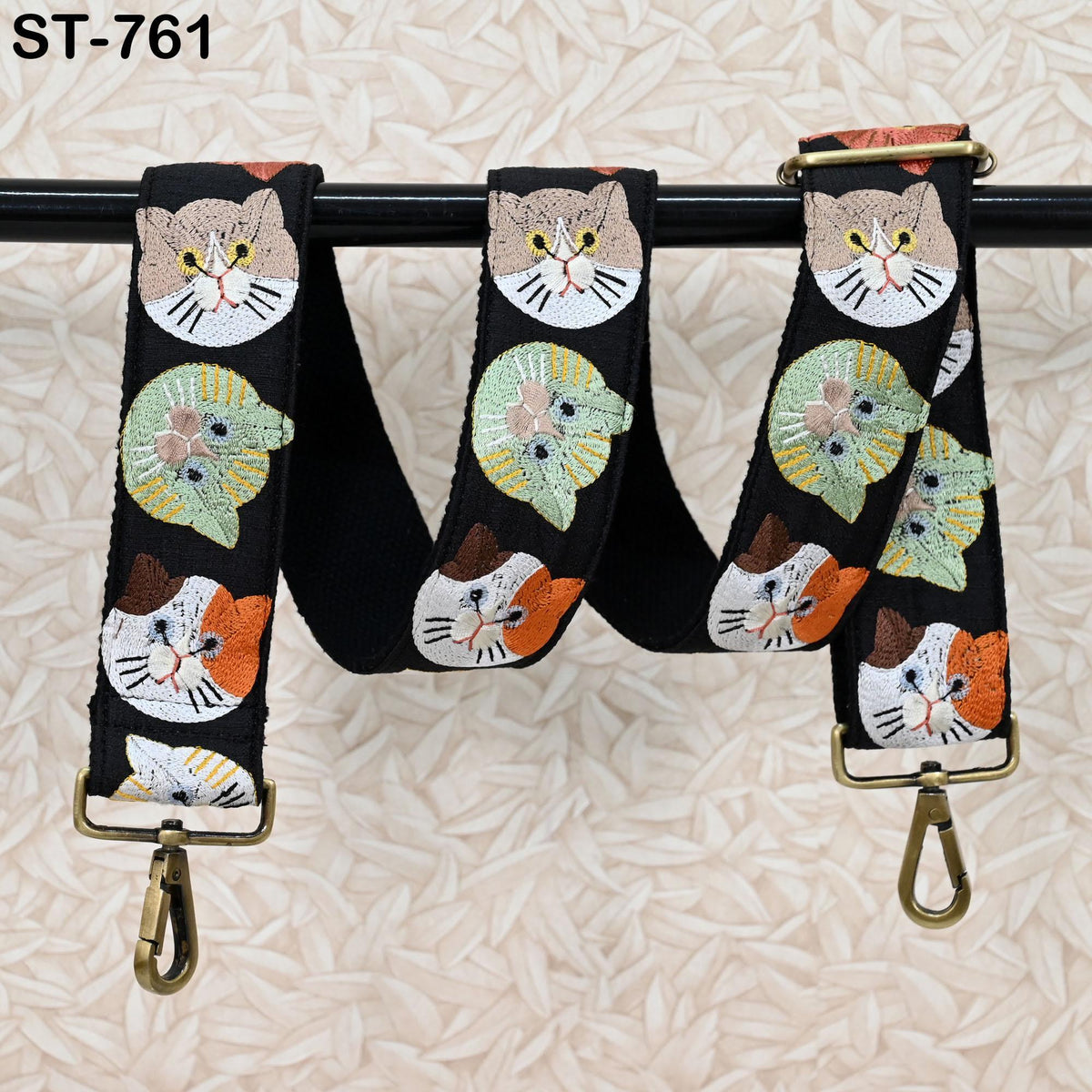A black strap with a repeating pattern of cat faces in various colors, including orange, green, and white, hanging from a hook.