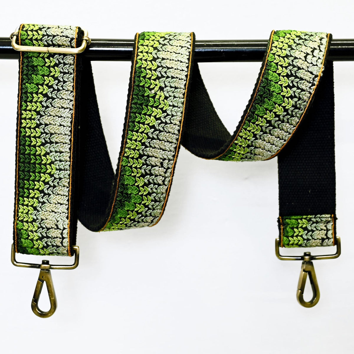 A green and black patterned strap with a metal hook attached, hanging on a black rod.