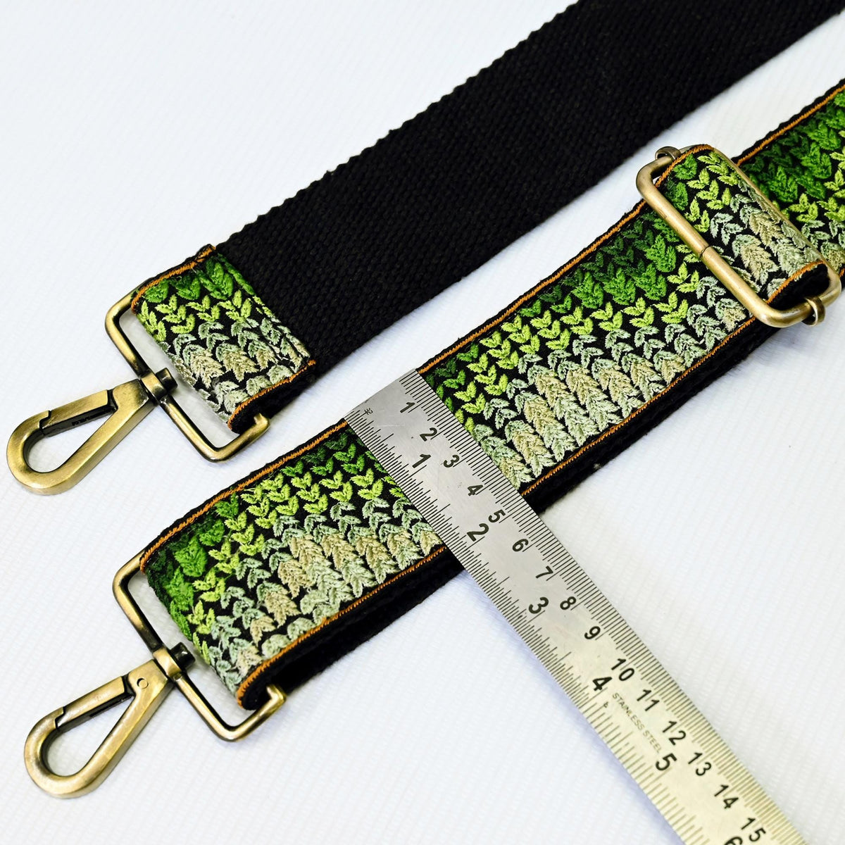 a black strap with a green and white patterned design, and a ruler placed next to it, indicating the strap's length.