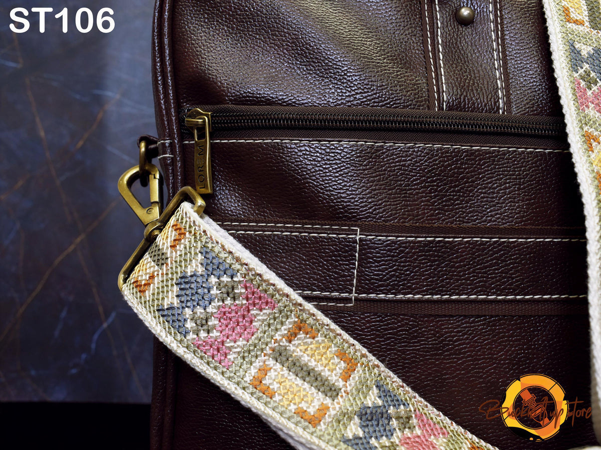 A close-up view of a brown leather bag with a colorful patterned strap, featuring a zipper closure and a metal clasp.