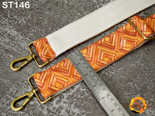 a white strap with an orange and yellow geometric pattern, and a metal ruler placed next to it on a textured surface.