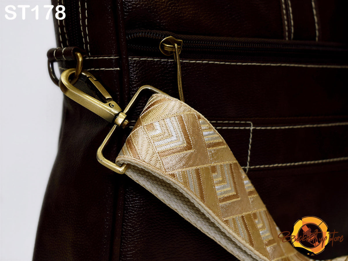 a close-up view of a brown leather bag with a gold-colored strap, featuring a zipper closure and a metal clasp.