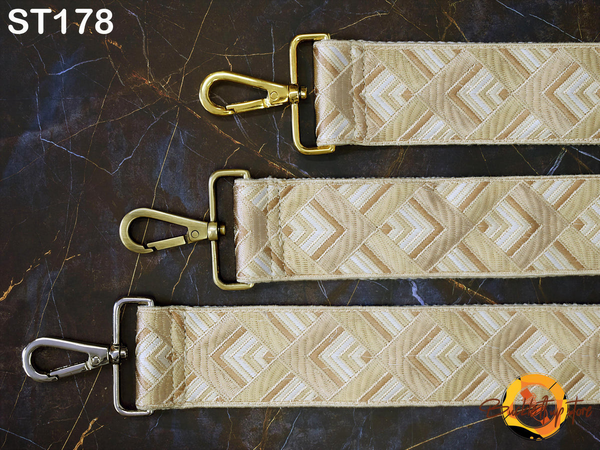 three straps with gold metal buckles and gold metal clasps, arranged on a dark marble surface.