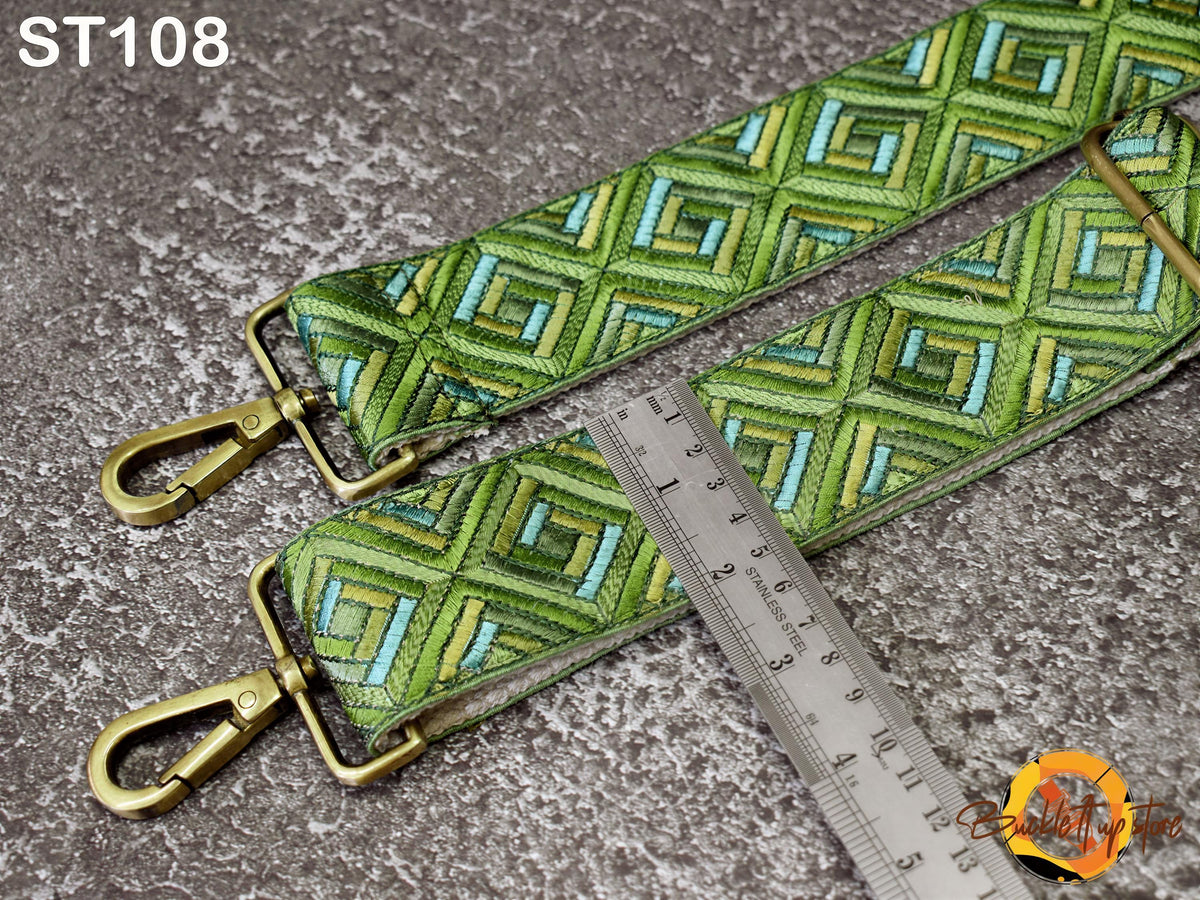 a green and gold patterned strap with a metal ruler placed next to it, indicating the strap's size or length.