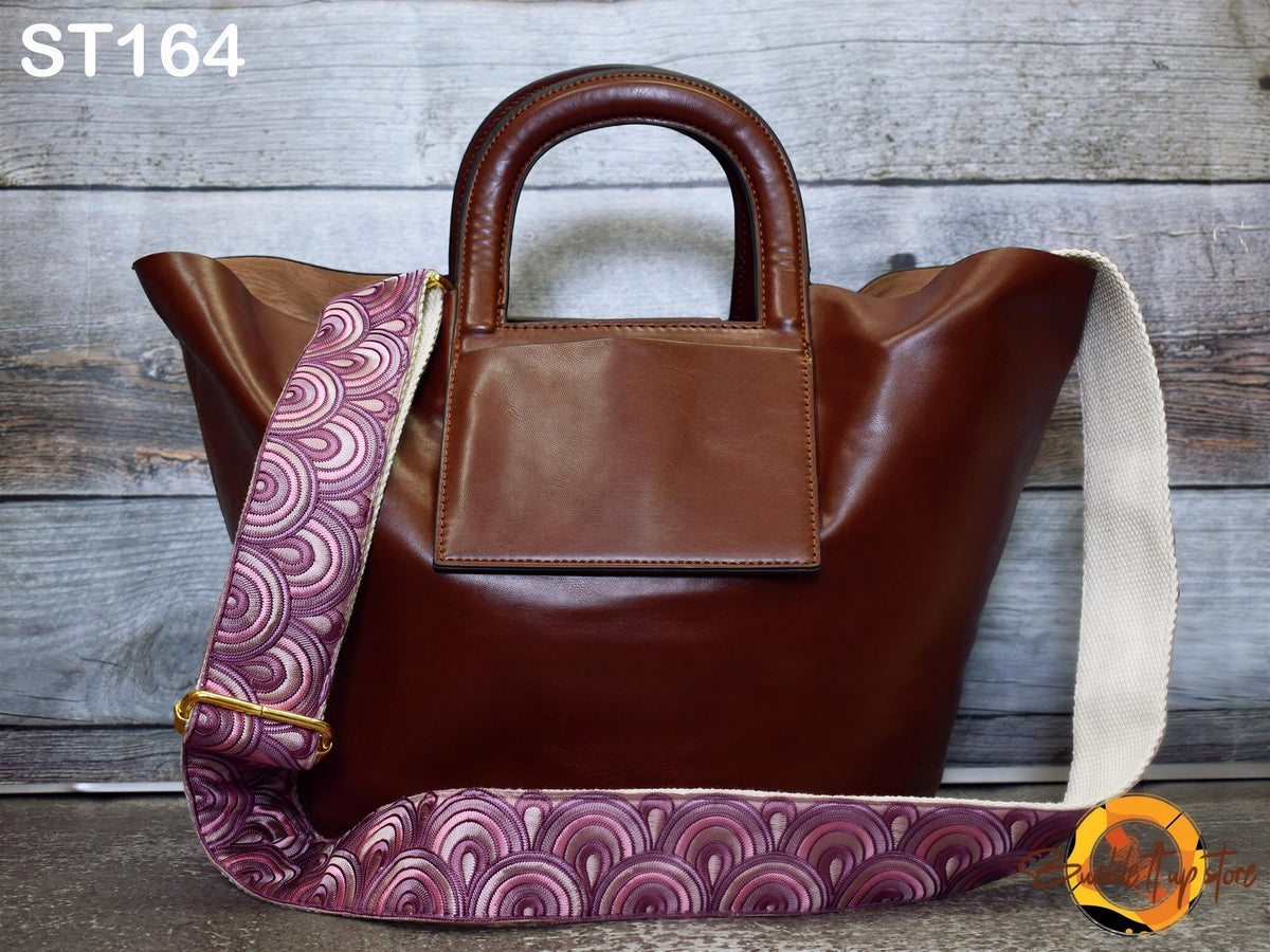 A brown leather handbag with a patterned strap is displayed against a wooden background.