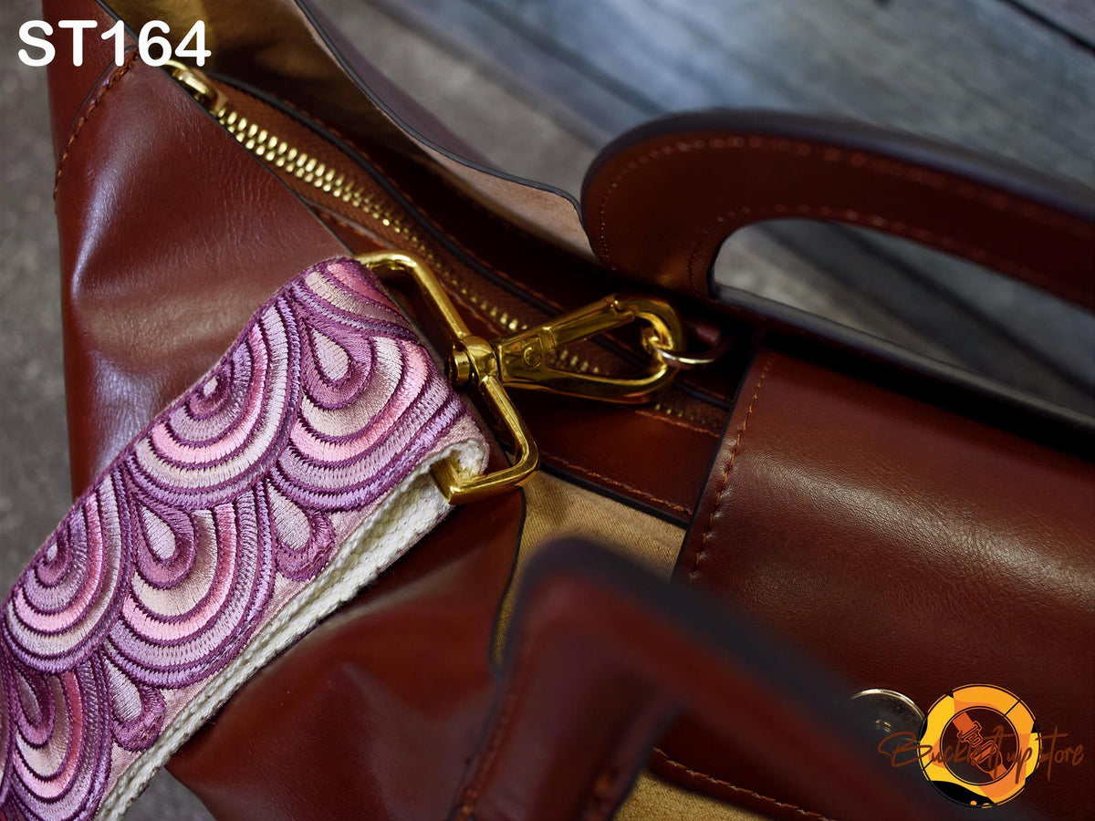 A close-up view of a brown leather handbag with a gold zipper and handle, featuring a decorative pattern on the strap.