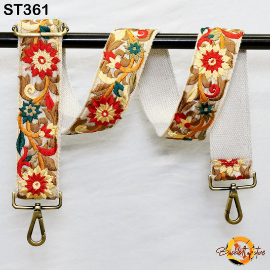 a white strap with a floral pattern and two metal hooks on the ends, hanging against a white background.