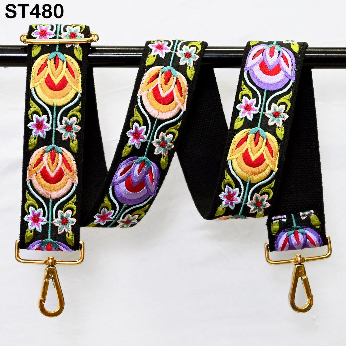 A colorful, embroidered strap with floral patterns in various shades of red, yellow, green, and purple. The strap is hanging from a black metal hook, with two gold metal hooks attached to the ends.
