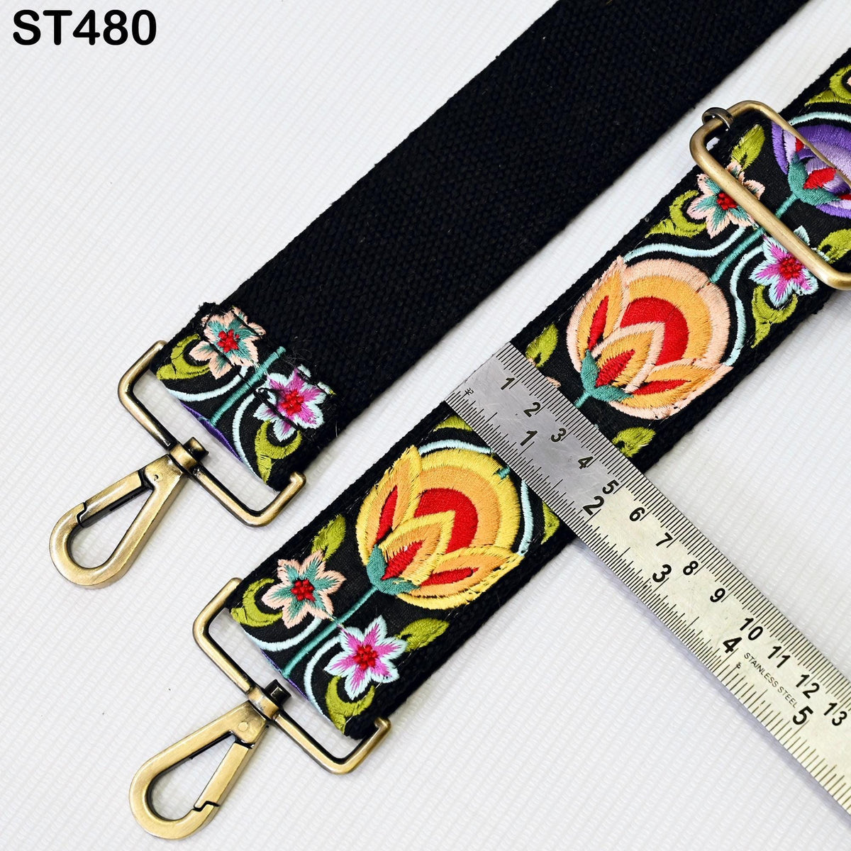 a black strap with colorful floral embroidery, and a ruler is placed next to it, indicating the strap's length.