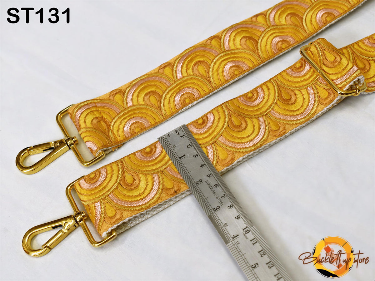 a gold-colored strap with a repeating pattern of circles and swirls, placed on a white surface. A ruler is placed next to the strap, indicating its size.