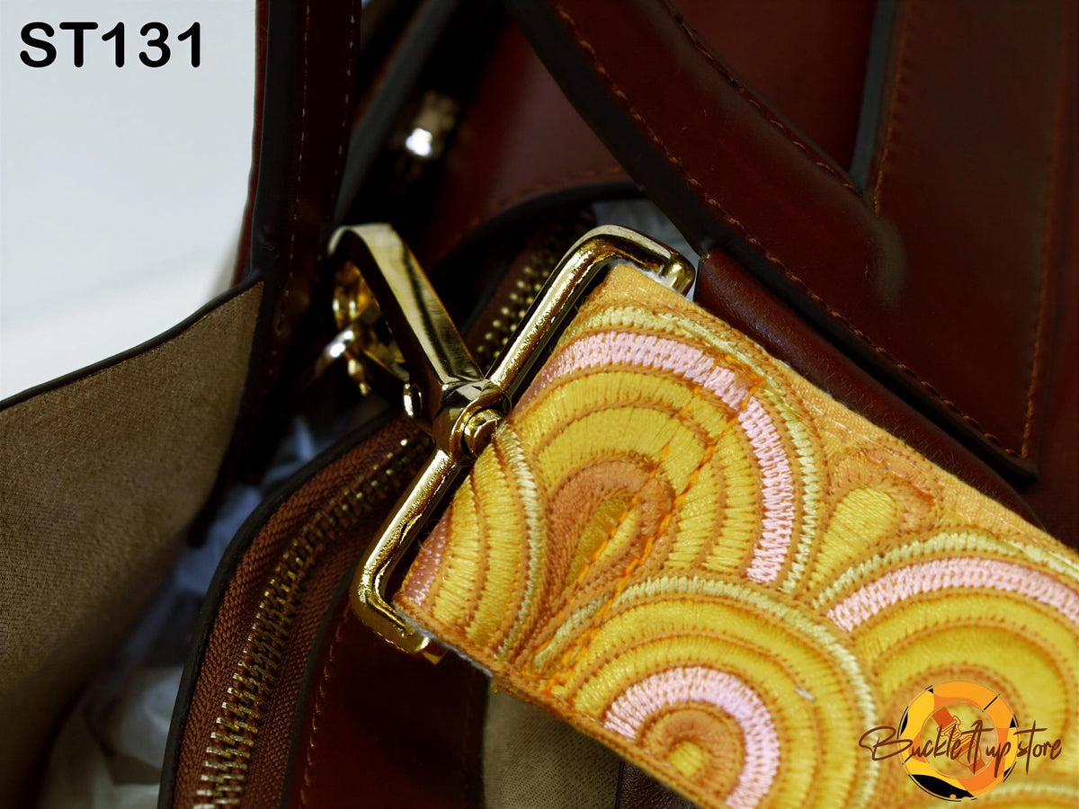 A close-up view of a brown leather handbag strap with a gold zipper pull and a decorative pattern on the strap.