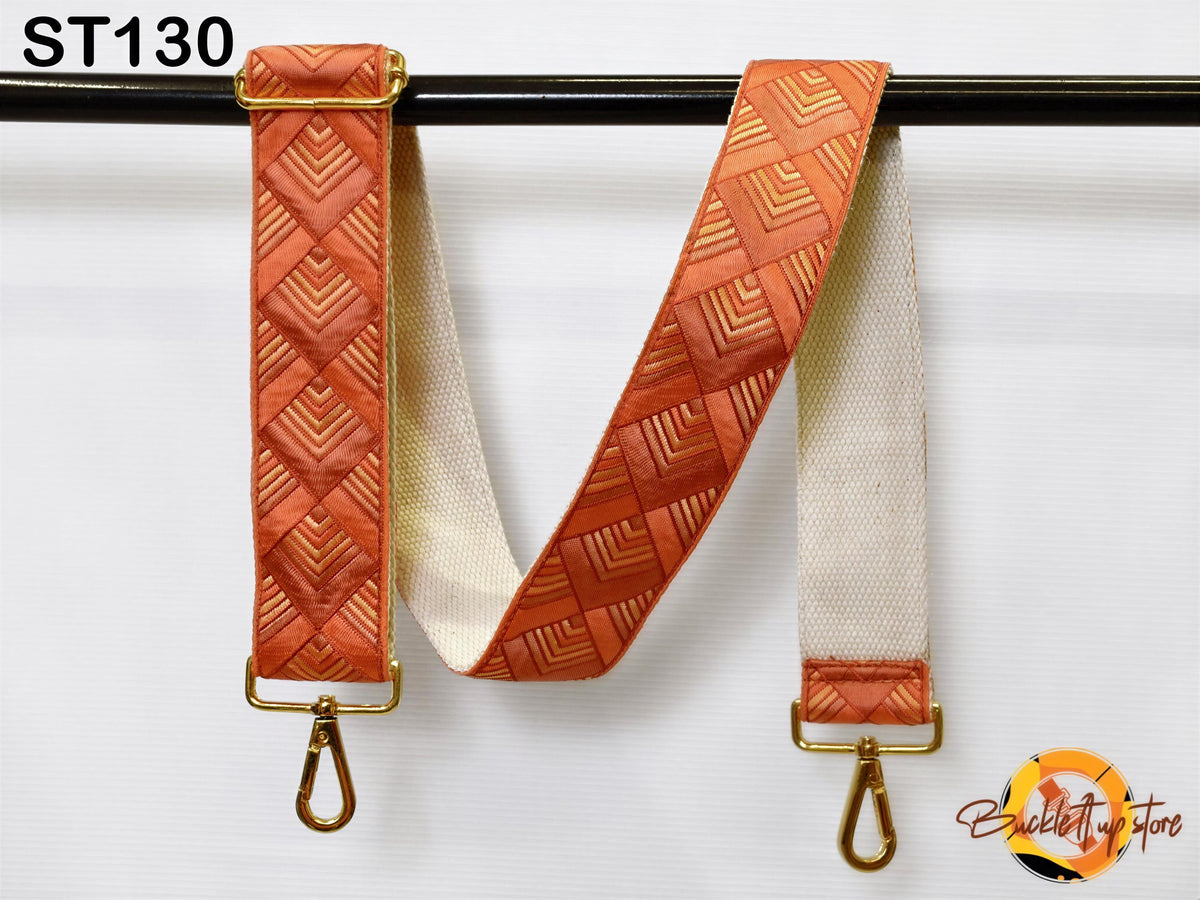 a strap with a geometric pattern in shades of orange and white, hanging on a black bar.