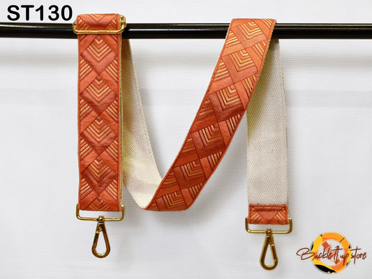 a strap with a geometric pattern in shades of orange and white, hanging on a black bar.