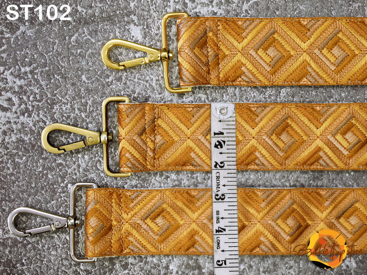 three straps with a geometric pattern in shades of yellow and gold, laid out on a gray surface.