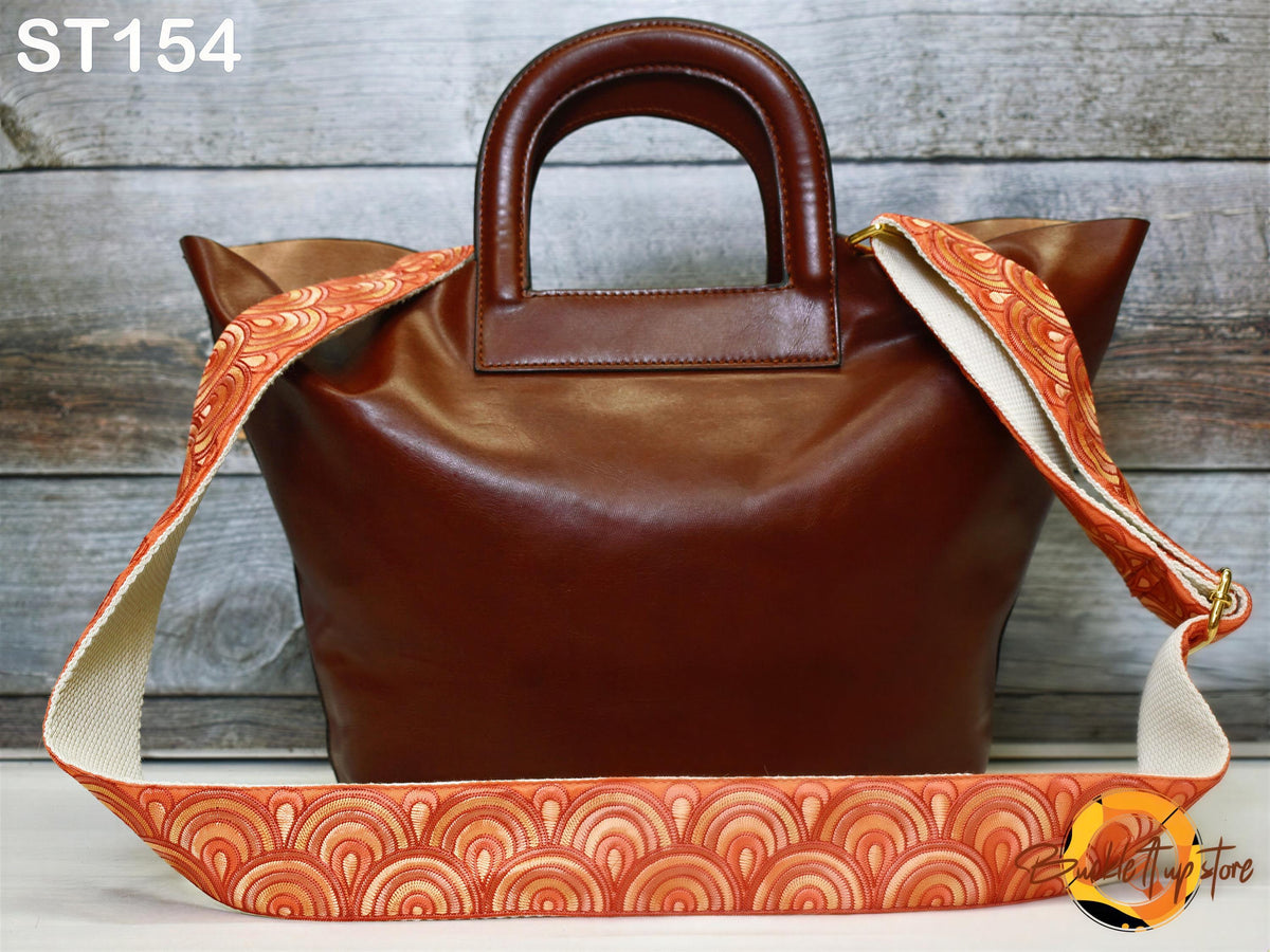 A brown leather handbag with a patterned strap is displayed against a wooden background.