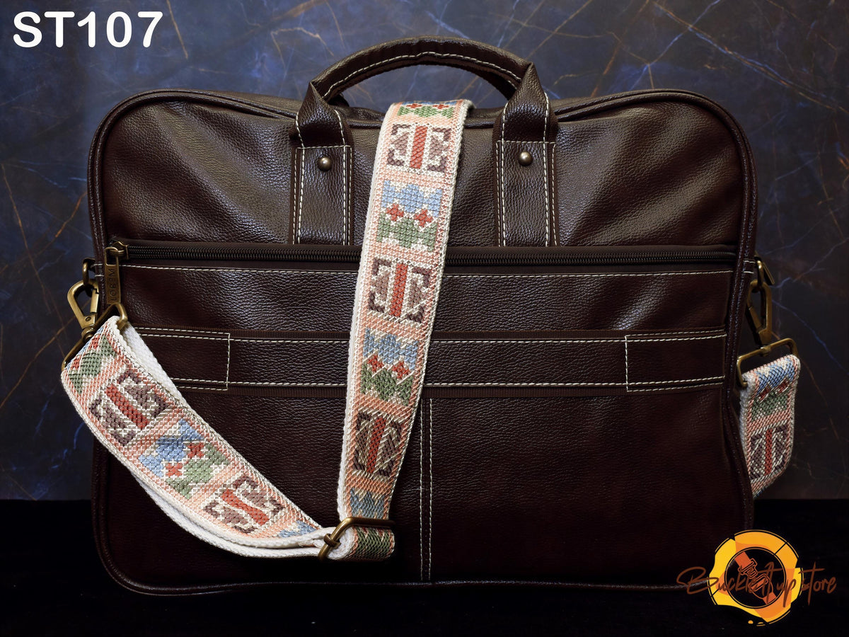 A brown leather laptop bag with a colorful patterned strap, placed against a dark background.