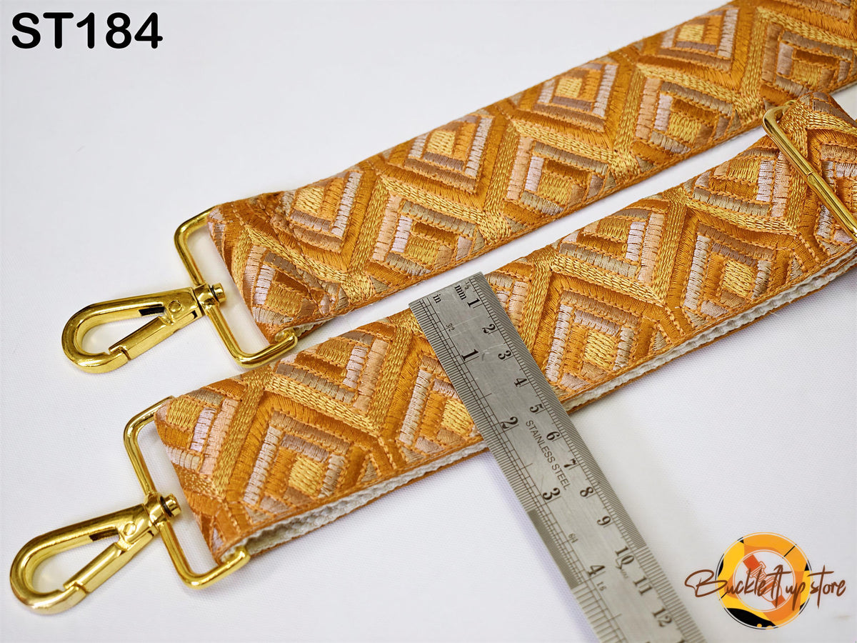 a close-up view of a gold-colored strap with a geometric pattern, placed next to a ruler for size comparison.