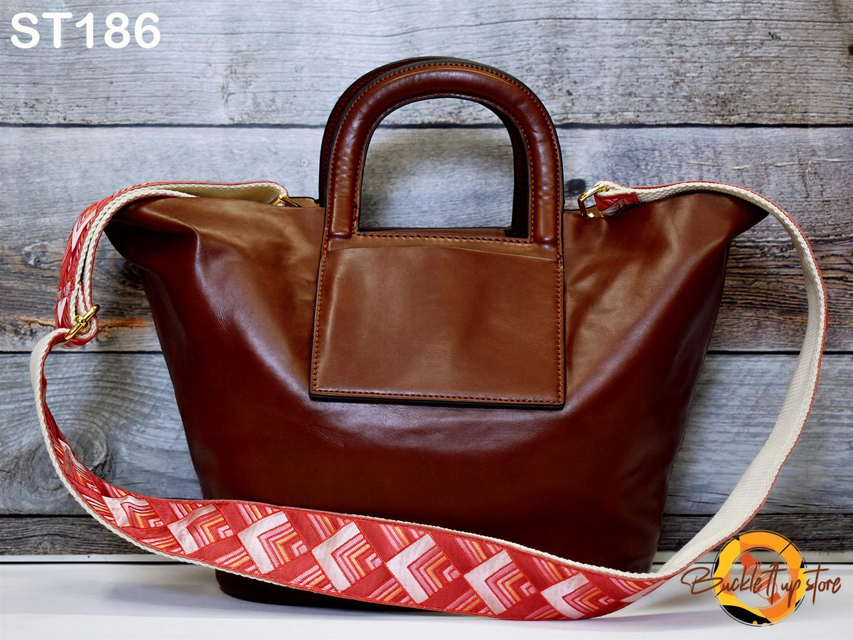 A brown leather handbag with a red and white patterned strap is displayed against a wooden background.
