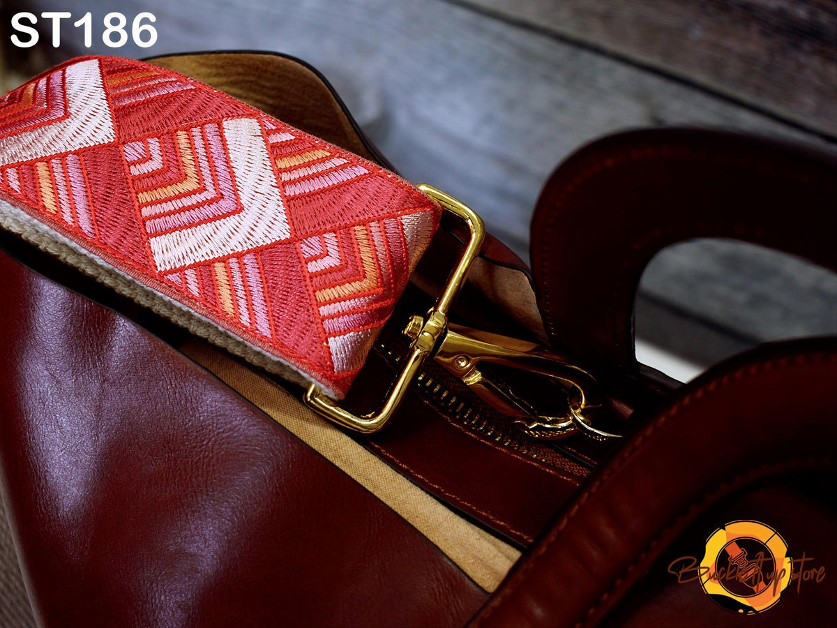 A close-up view of a brown leather handbag with a red and white patterned strap, resting on a wooden surface.