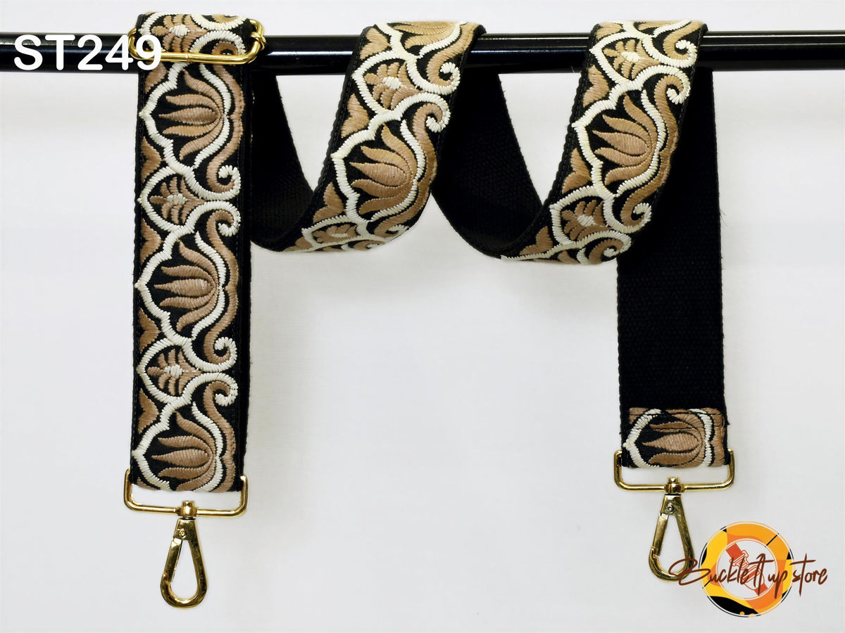 A black and gold strap with an intricate floral pattern, hanging from a black metal hook.