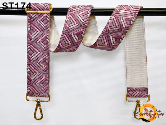 A strap with a geometric pattern in shades of pink and white, hanging on a black rod.