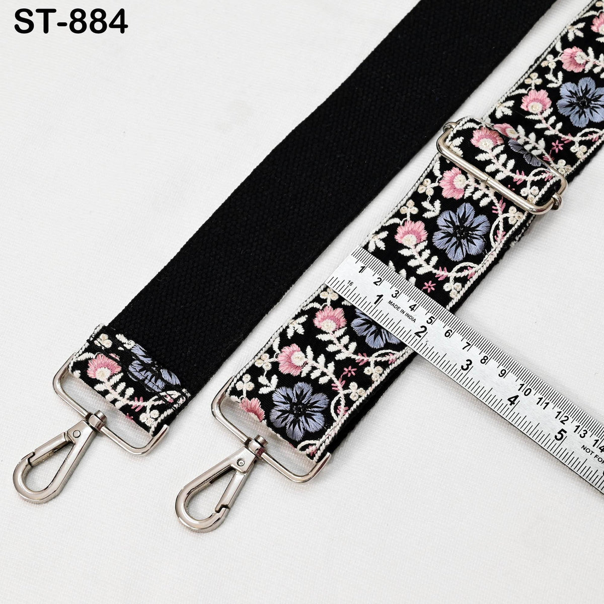a black strap with a floral pattern and two metal hooks, accompanied by a ruler for size comparison.