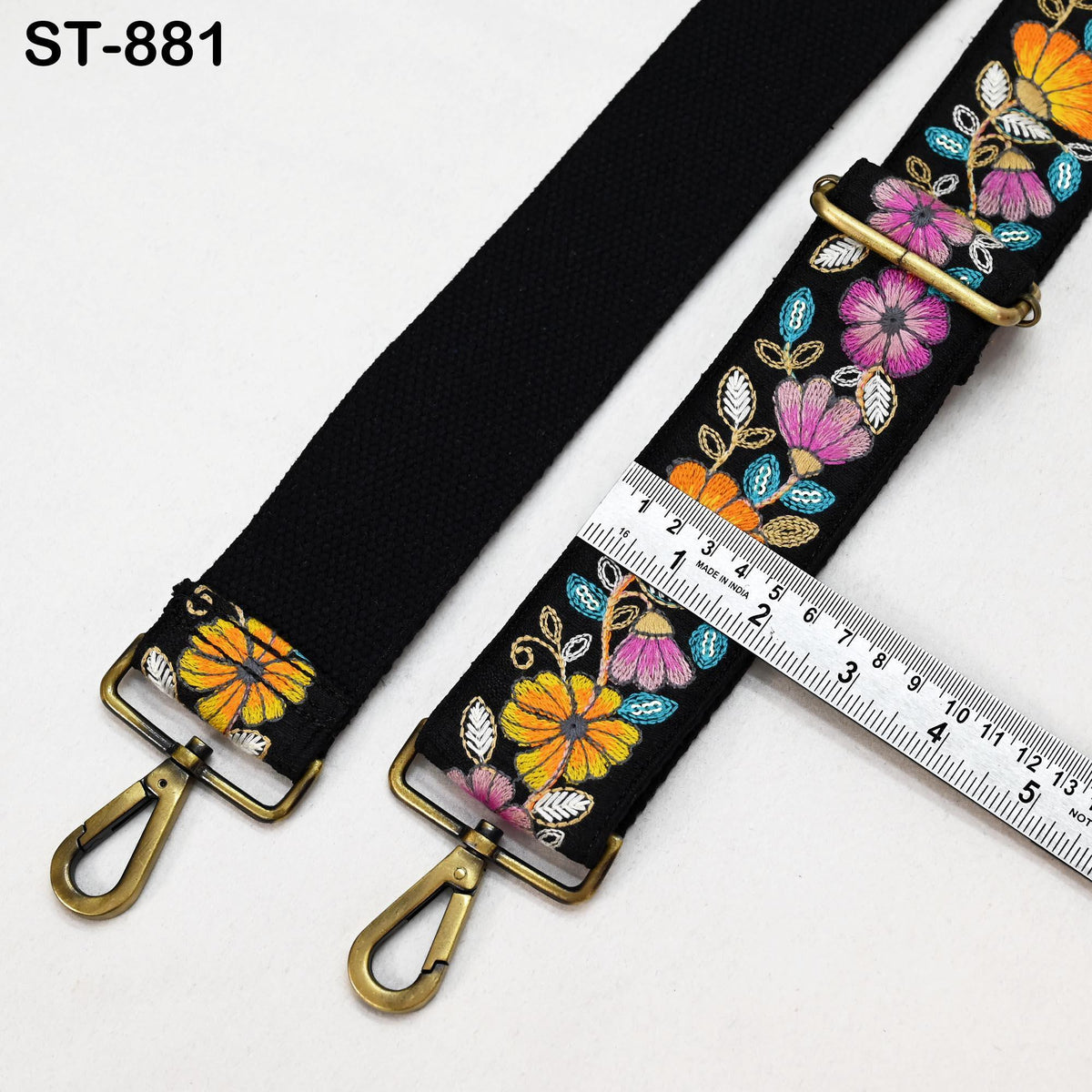 a black strap with colorful floral embroidery, and a ruler is placed next to it, indicating the strap's length.