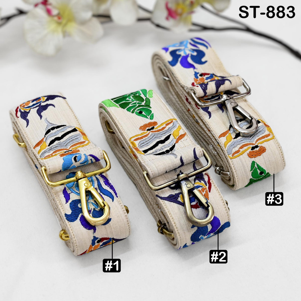 Three colorful fabric straps with metal hooks, each with a unique pattern, are displayed on a white surface.