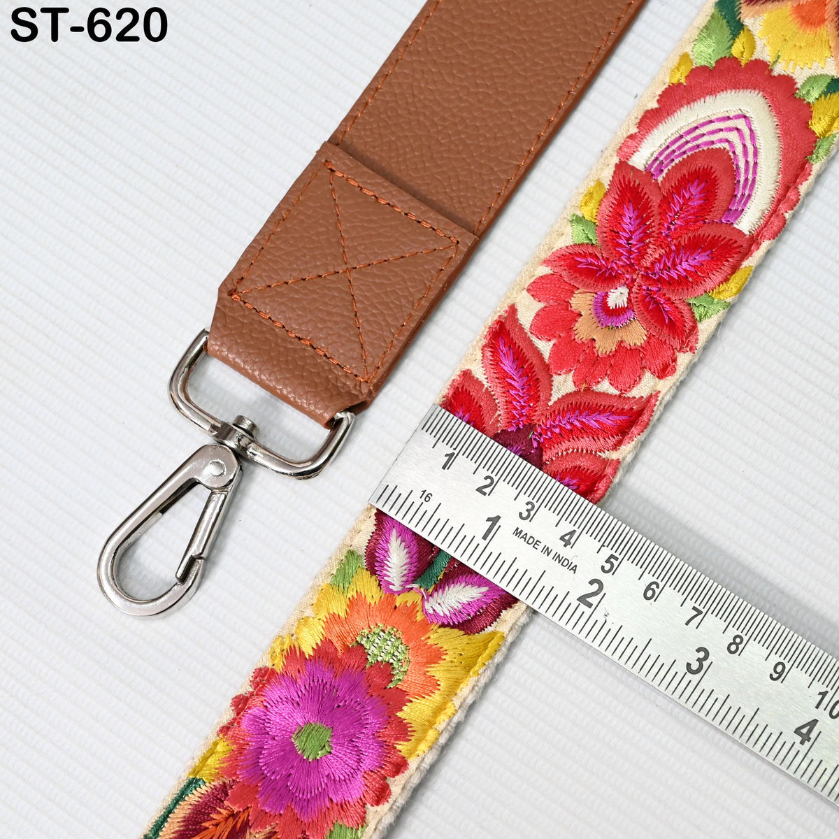 a brown leather strap with a floral pattern and a metal hook, placed next to a ruler for size comparison.