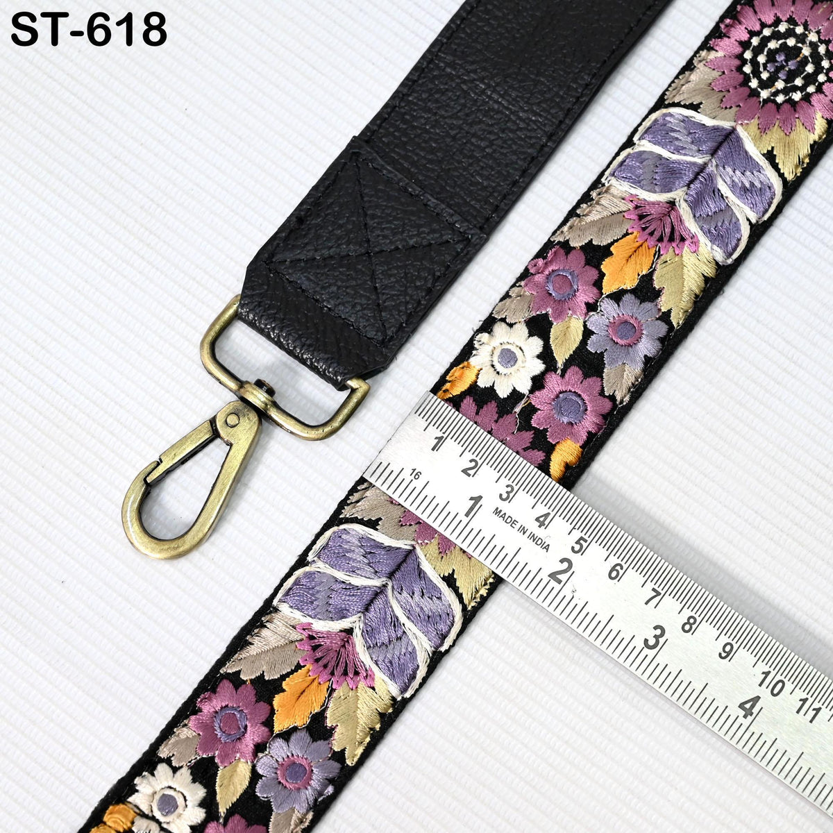 a black leather strap with a floral pattern, and a ruler is placed next to it, indicating the strap's length.