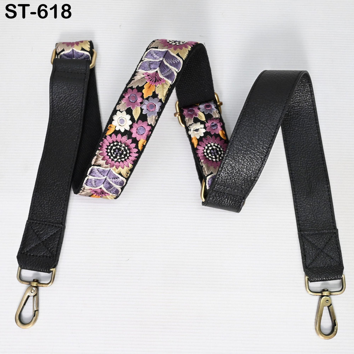 A floral patterned leather strap with a black leather strap attached to it, both with gold buckles.