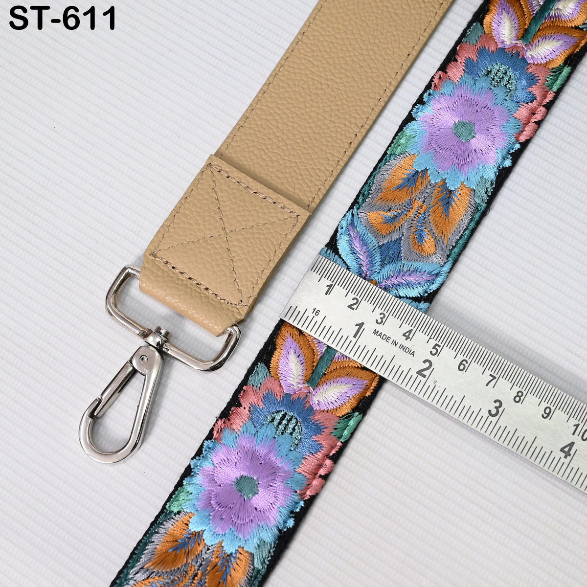 a beige strap with a floral pattern and a metal hook, placed next to a ruler for size comparison.