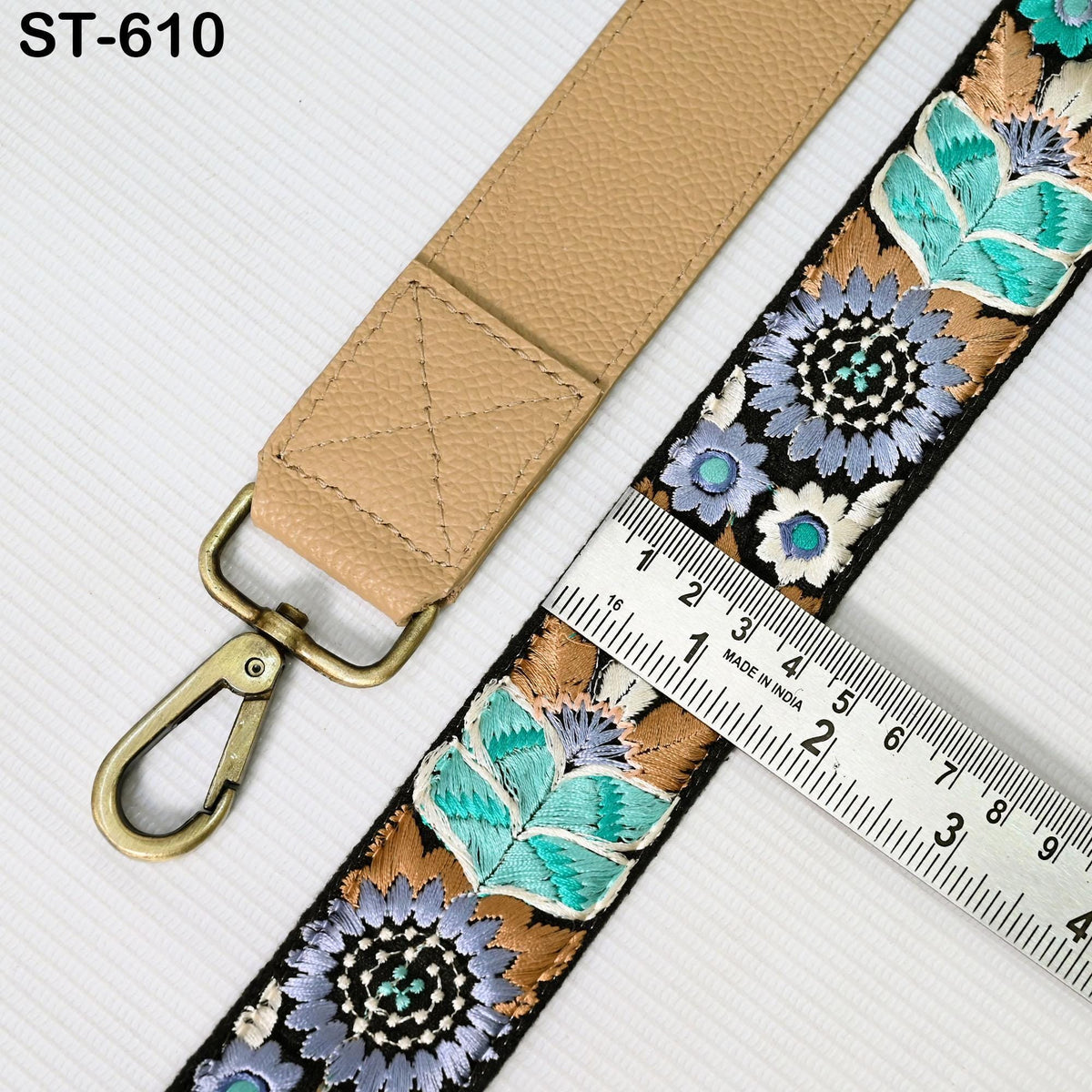 a beige strap with a floral pattern and a metal clasp, placed next to a ruler for size comparison.
