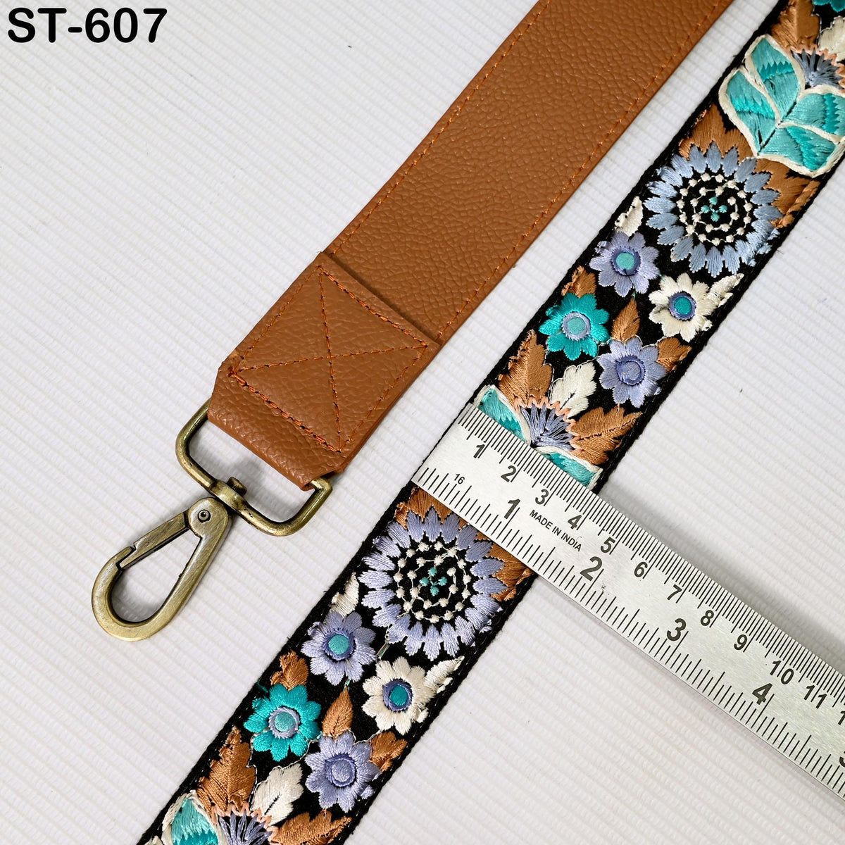 a brown leather strap with a floral pattern, placed next to a ruler for size comparison.