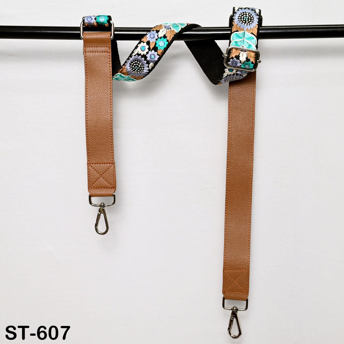 A brown leather strap with a floral pattern hanging from a black bar.